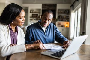 Two people discussing documents at a table with a laptop