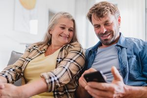 Two people sitting on a couch smiling while looking at a smartphone together
