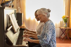 Two women play the piano together at home.