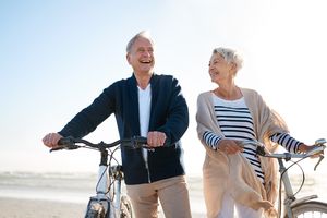 Retired couple smiling and walking their bikes on a beach
