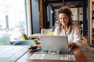 A person seated at a table in a cafe working on a laptop smiling