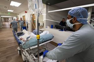 Healthcare workers push a patient on a stretcher in a hospital corridor with additional staff visible in the background