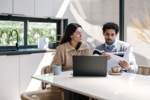 Two individuals reviewing documents sitting at a table with a laptop and coffee cups